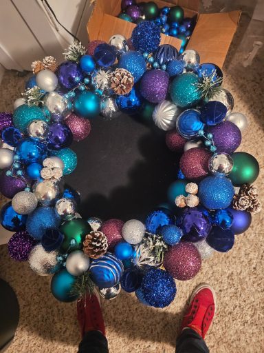 Colorful holiday wreath adorned with various ornaments in blue, purple, and silver.