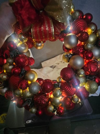 A festive holiday wreath adorned with red, gold, and silver ornaments and lights.