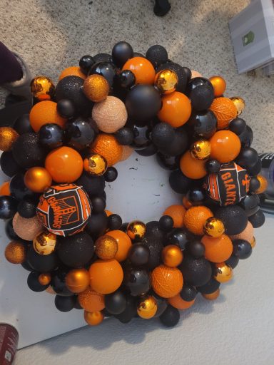A circular wreath made of black, orange, and gold ornaments.